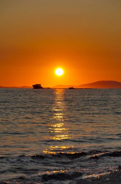 Gün batımında deniz suyunda küçük tekneleri olan huzurlu deniz manzarası, sıcak altın ışık ve yansımalar huzurlu ve zamansız bir atmosfer yaratır, yolculuk, doğa ve rahatlama temaları için mükemmeldir.