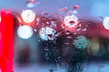 Işıkların arka planına karşı bir SUV 'nin camına yağmur damlaları