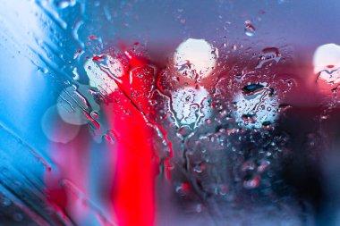 Işıkların arka planına karşı bir SUV 'nin camına yağmur damlaları