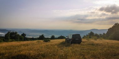 SUV bir yaz akşamı vadiye bakan dağlık bir alanda seyahat eder.
