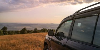 SUV bir yaz akşamı vadiye bakan dağlık bir alanda seyahat eder.