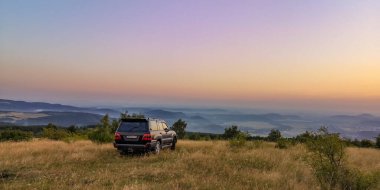SUV bir yaz akşamı vadiye bakan dağlık bir alanda seyahat eder.