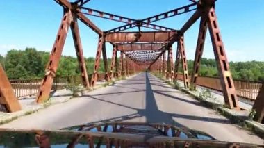 Bir dağ nehri üzerindeki demir bir köprüde bir off-road aracı sürüyor.