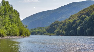 Uzaktaki bir grup insan bir dağ nehrinde katamaranların üzerinde yüzüyor.