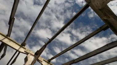 Eski çiftliğin yıkılmış çatısının beton kirişlerinde parlayan bulutlarla mavi gökyüzü.