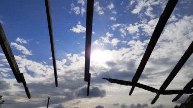 Eski çiftliğin yıkılmış çatısının beton kirişlerinde parlayan bulutlarla mavi gökyüzü.