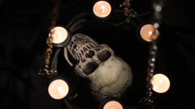 Zincire vurulmuş mumlarla çevrili aptal insan kafatası.