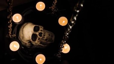 Zincire vurulmuş mumlarla çevrili aptal insan kafatası.