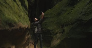 Bir adam vadide dikiliyor ve akıllı telefondan video çekiyor. Sırtında büyük bir sırt çantası var. Dağlarda yürüyüş. 4K DCI