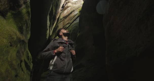 男が峡谷に立って山を見上げている。彼は背中に大きなリュックを持っている。下から撮影。山の中でハイキング。4K DCI — ストック動画