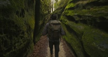Bir adam vadide yürüyor. O, büyük bir sırt çantası taşıyor. Kayaların etrafında yosun var. Arkadan ateş ediyorlar. Dağlarda yürüyüş. 4K DCI