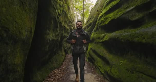 Un homme marche dans la gorge et sourit. Il porte un grand sac à dos. Il regarde la nature qui l'entoure. Randonnée dans les montagnes. ICD 4K — Video