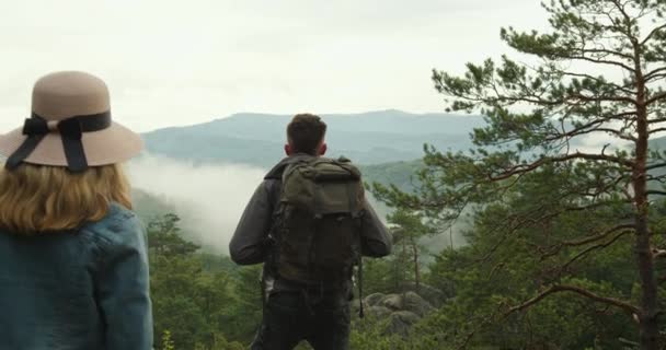 A nő közeledik a férfihoz. Egy szikla tetején állnak, és a természetet nézik. Túrázás a hegyekben. 4K DCI — Stock videók