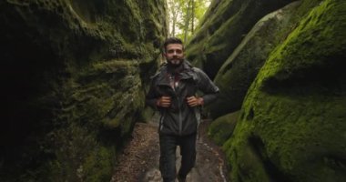 Bir adam vadide yürüyor ve gülümsüyor. O, büyük bir sırt çantası taşıyor. Dağlarda yürüyüş. 4K DCI