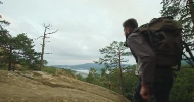 Bir adam uçurumun tepesine çıkıyor ve manzaraya bakıyor. O, ellerini kaldırıyor ve mutlu. Dağlarda yürüyüş. 4K DCI