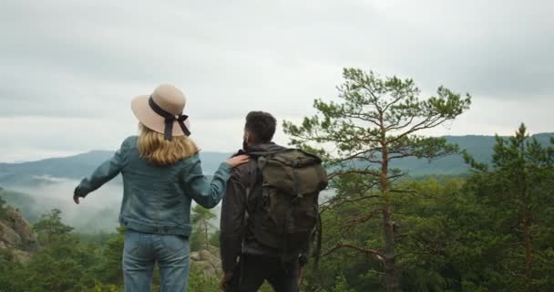 Een vrouw en een man staan op een klif en kijken naar de natuur. Wandelen in de bergen. 4K DCI — Stockvideo