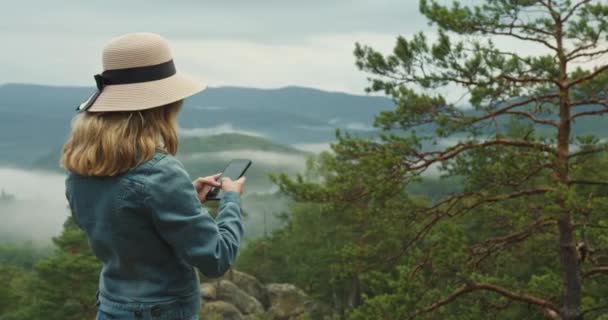 Eine Frau steht auf einer Klippe und schreibt eine Nachricht auf ihr Smartphone. Wandern in den Bergen. 4K DCI — Stockvideo