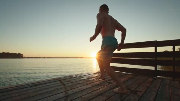 Genç bir adam göle atlıyor. Gölde dinlen. Gün batımı. 4K — Stok video