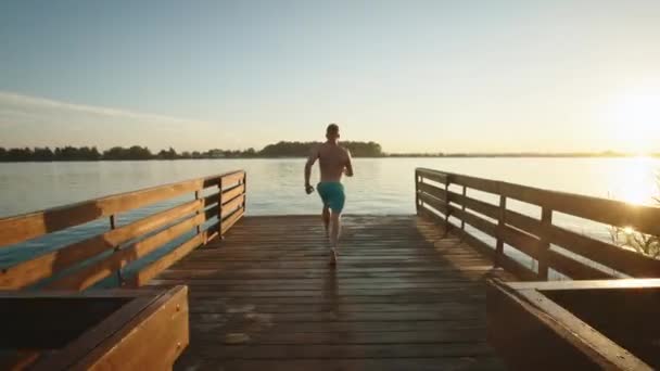 Genç bir adam iskelede koşuyor ve bir bomba gibi göle atlıyor. Gölde dinlen. Gün batımı. 4K — Stok video