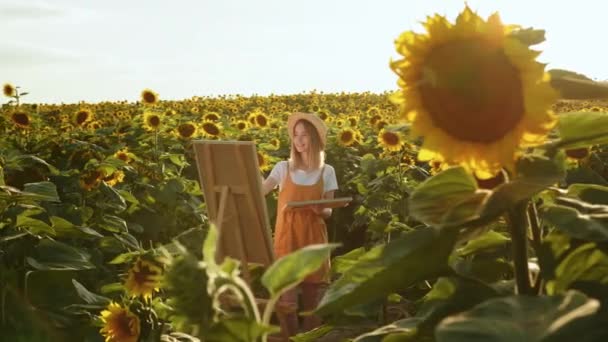 Kobieta stoi na polu słoneczników i rysuje obraz. Uśmiecha się. Artysta w naturze. 4K — Wideo stockowe