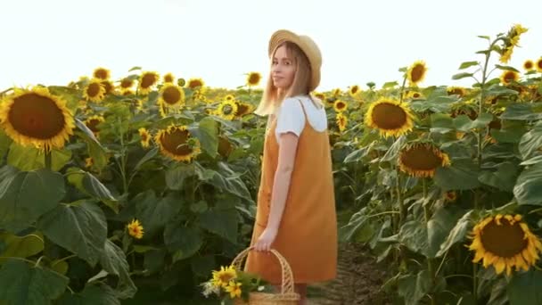 Žena s košíkem květin se dívá do kamery a usmívá se. Stojí mezi slunečnicemi. 4K — Stock video