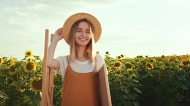 Kadın gülümsüyor. O, ayçiçeklerinin arasında bir sehpanın yanında duruyor. 4K
