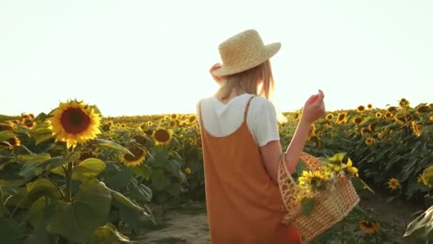 Uśmiechnięta kobieta niesie kosz kwiatów. Krąży w polu słoneczników. 4K — Wideo stockowe