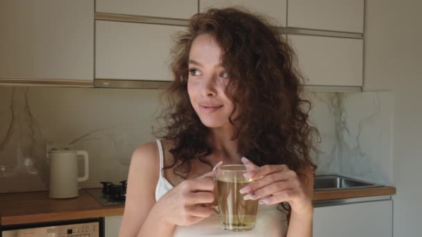 若い女性が窓から外を見てお茶を飲んでいる。朝の太陽が輝いている。4K — ストック動画