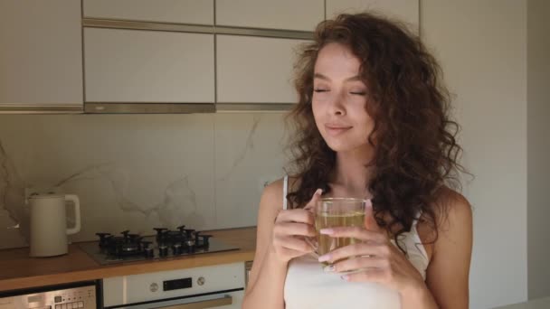 女がお茶を飲んでいる。彼女は窓の外を見ている。朝の太陽が輝いている。4K — ストック動画