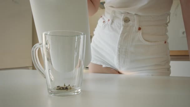 Uma jovem está derramando água em um copo de um bule de chá. Tiroteio de perto. 4K — Vídeo de Stock