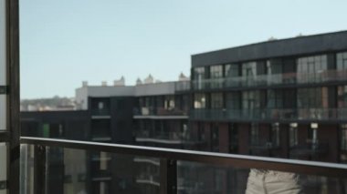 Genç bir kadın dairesinin balkonuna çıkıyor. Elinde bir fincan kahve tutuyor. Güneş dışarıda pırıl pırıl parlıyor. 4K