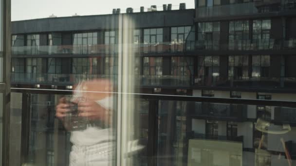 Een jonge en mooie vrouw gaat het balkon op. Ze houdt een kop koffie vast. 4K — Stockvideo