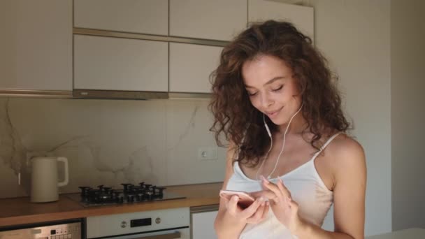Uma mulher está a gostar de música. Ela está de pé na cozinha e dançando. 4K — Vídeo de Stock