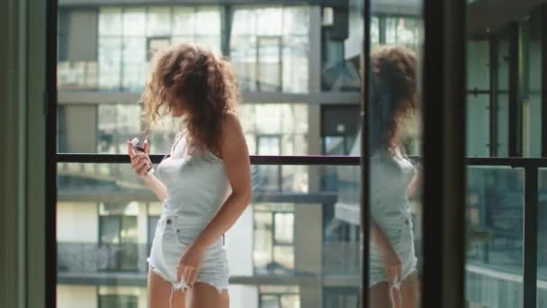 若い美しい女性がバルコニーに立っている。彼女は音楽を聴いて体をよく動かしている。4K — ストック動画
