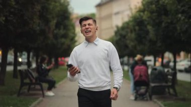 Bir adam yürüyor ve kulaklıkla müzik dinliyor. O şarkı söylüyor. 4K