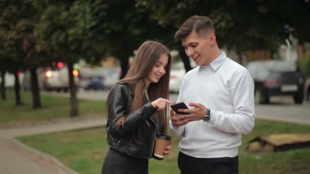 Мужчина показывает фотографию на смартфоне молодой женщине. Они улыбаются и разговаривают. 4K — стоковое видео