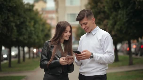 Uma jovem e um homem estão trocando informações sobre smartphones. Estão a sorrir. 4K — Vídeo de Stock