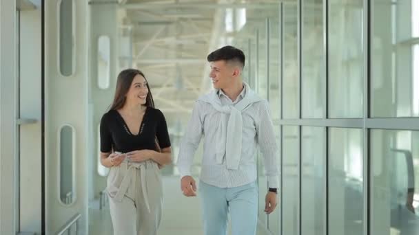 Egy fiatal nő és egy férfi beszélgetnek és sétálnak a reptéren. Viccelnek és mosolyognak. 4K — Stock videók