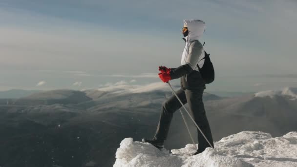Een jonge vrouw staat op de rand van een met sneeuw bedekte klif en kijkt naar het landschap. Ze houdt wandelstokken in haar handen. De berg Pikui. 4K — Stockvideo