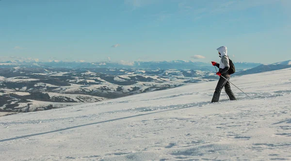 Genç bir kadın karla kaplı bir dağda yürüyor. İniş için yürüyüş çubuklarını kullanıyor. Arka planda karla kaplı dağlar. Pikui Dağı.