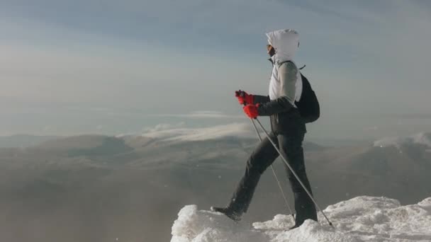 若い女性は雪に覆われた崖の端に立っており、風景を見ている。強い風が吹いて彼女を吹き飛ばす。ピクイ山。4K — ストック動画