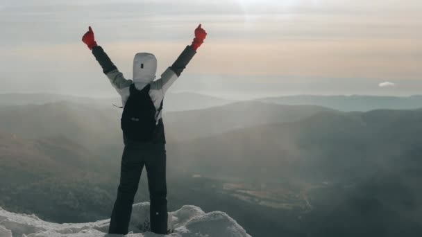 En ung kvinna står på kanten av ett snötäckt berg. Hon sträcker upp sina händer och gläds åt att hon har erövrat detta berg. Hon tittar på landskapet. Pikui-berget. 4K — Stockvideo