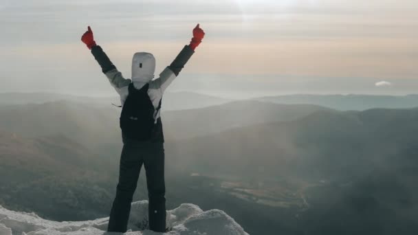 Una joven está de pie al borde de una montaña nevada. Ella levanta las manos y se alegra de haber conquistado esta montaña. Ella está mirando el paisaje. Monte Pikui. 4K — Vídeo de stock