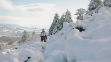Genç bir kadın yavaşça karlı bir dağın tepesine tırmanıyor. O, yürüyüş çubuklarıyla ellerinde yükseliyor. Arka planda karla kaplı dağlar. Pikui Dağı