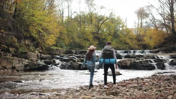 Une jeune femme et un homme marchent le long du rivage rocheux d'une rivière de montagne. Randonnée dans les montagnes. 4K — Video