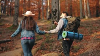 Genç bir kadın ve bir adam sonbahar ormanında yürüyorlar. El ele tutuşuyorlar. Konuşuyorlar ve gülümsüyorlar. Dağlarda yürüyüş. 4K