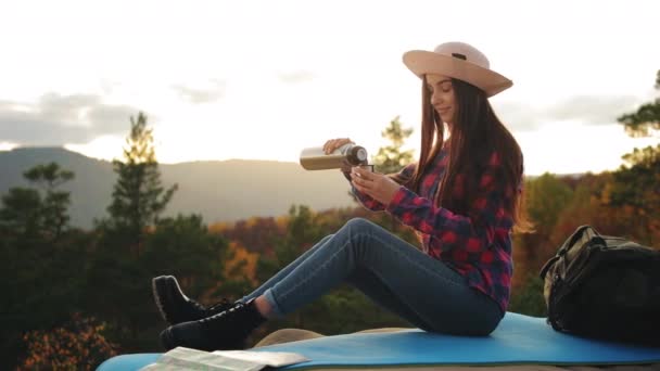Mladá žena si nalévá čaj z termosky. Sedí na skále. Krásný západ slunce. Turistika v horách. 4K — Stock video