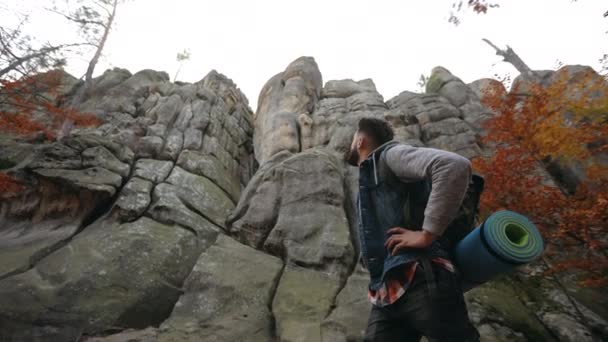 Un homme se tient au fond d'un gros rocher. Il regarde les rochers. Randonnée dans les montagnes. 4k — Video