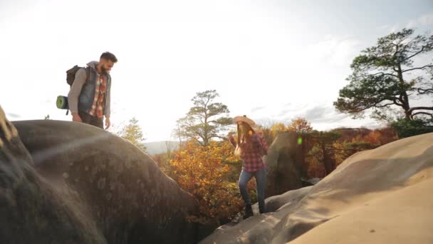 En ung kvinna klättrar uppför en klippa. Han hjälper henne. Vacker solnedgång. Vandring i bergen. 4K — Stockvideo