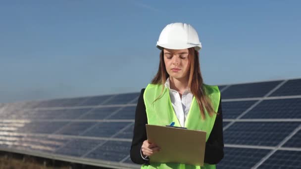 Bir kadın mühendis güneş panellerini inceliyor ve verileri belgelere kaydediyor. 4k — Stok video